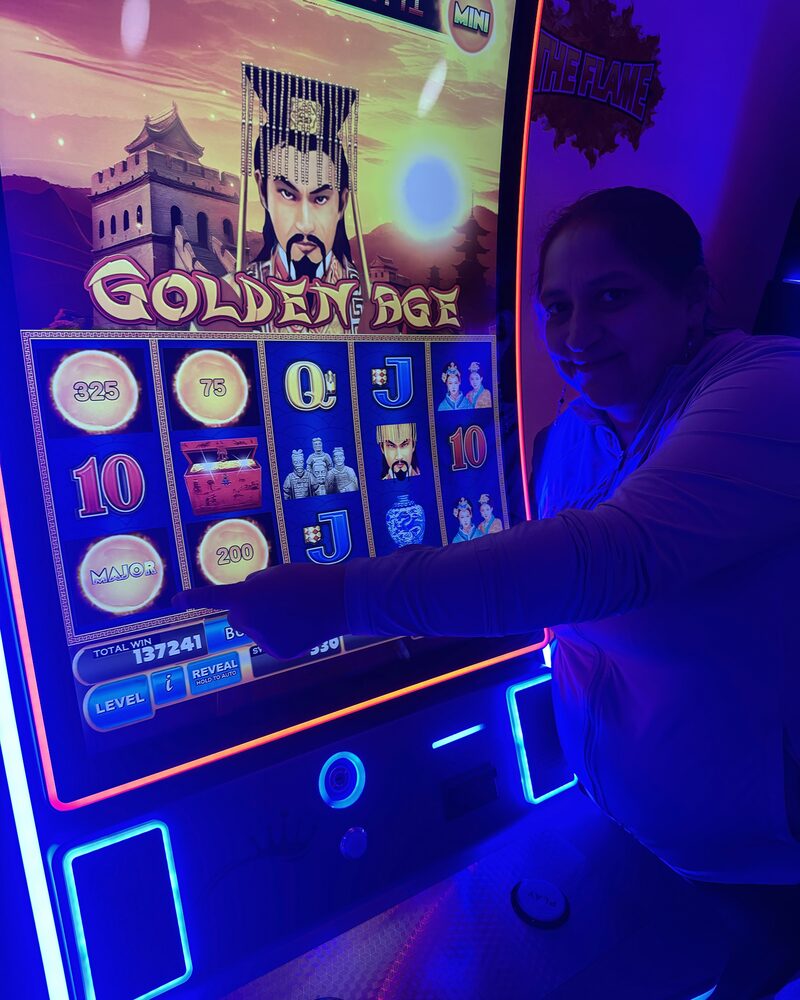 A guest at The Flame smiling beside a Golden Age game screen showing her winning total